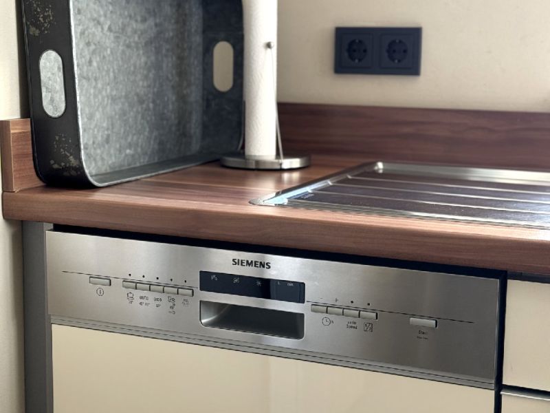 Detailaufnahme der modernen Küche der Ferienwohnung mit Abtropffläche aus Edelstahl und hochwertigem Geschirrspüler in stilvoller Holzoptik.
