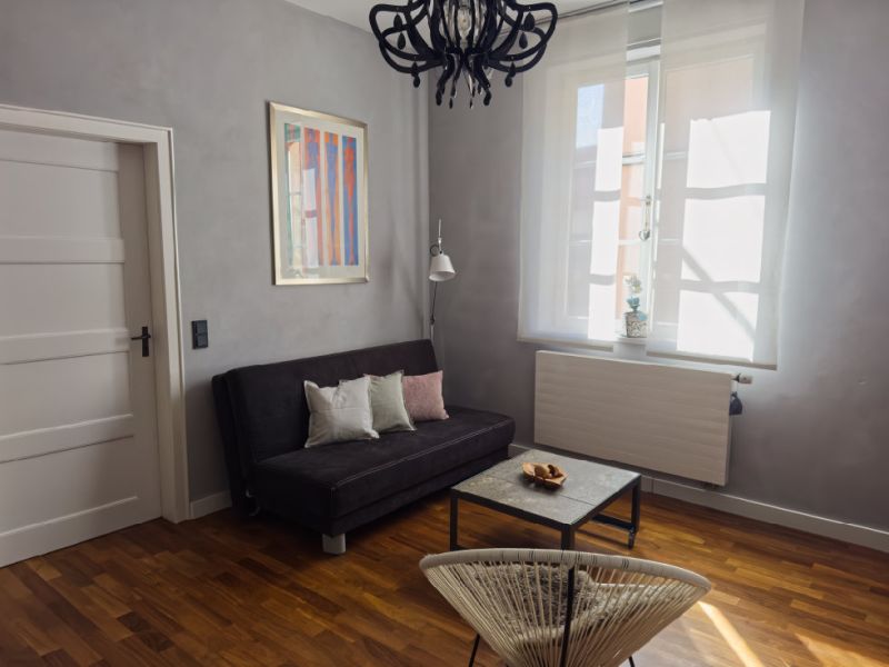 Stilvoll eingerichteter Wohnbereich der Ferienwohnung mit Sofa, Couchtisch, großen Fenstern und modernem Design in historischem Altstadtflair.